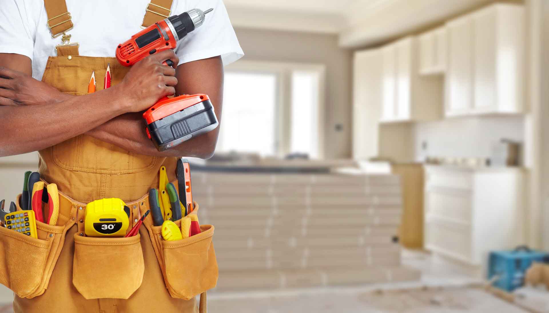Handyman poses with a power drill in front of an in-progress kitchen remodel