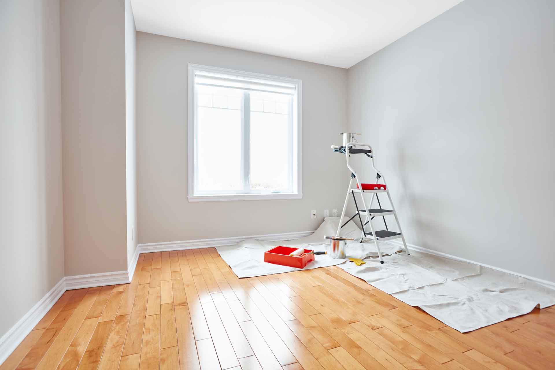 A ladder and paint is set up in an empty room