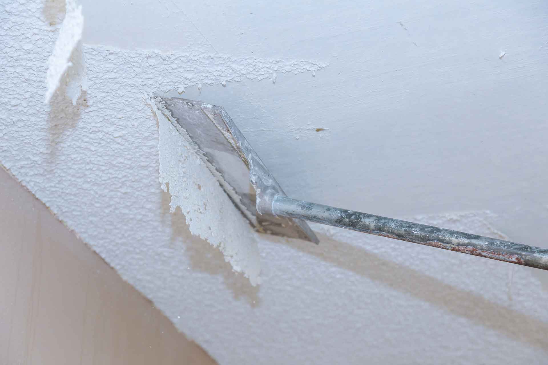 Handyman scrapes popcorn detailing off of ceiling